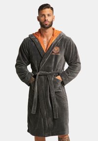 Grijs, gestructureerd badjasje met een oranje voering in de capuchon, een ceintuur in de taille en voorzakken. Heeft een logo op de borst geborduurd in het oranje.