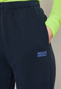 Pantalons de survêtement bleu marine avec une finition texturée, dotés d'une taille élastique et d'une poche externe. Logo "American Vintage" en bleu sur le devant.