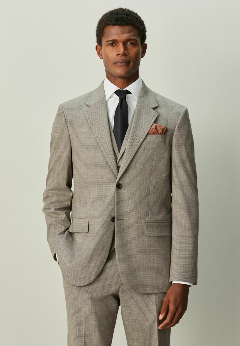 Traje de cuadros gris con chaqueta entallada y pantalones a juego. Incluye camisa blanca, corbata negra y pañuelo de bolsillo marrón.