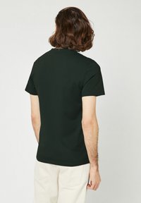 Donkergroen T-shirt met korte mouwen, ronde hals en een gladde katoenstructuur. Eenvoudig ontwerp, minimale naden en een ontspannen pasvorm.