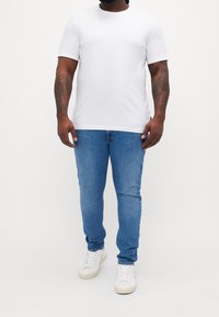 Bílý tričko s krátkým rukávem ve fitted designu, kombinované s světle modrými džíny a bílými teniskami. Jednoduchá, hladká textura, bez vzorů.