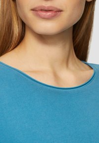 Blaues Baumwoll-T-Shirt mit weitem Rundhalsausschnitt. Glatte Textur mit kurzen Ärmeln, eng anliegend am Kragen und weicher Stoff.