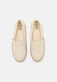 Scarpe slip-on in tela color beige con superficie testurizzata, scollatura elasticizzata a V e suola in corda di juta naturale. Etichetta del marchio visibile all'interno della scarpa.
