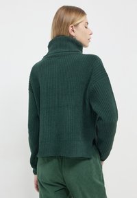 Grüner strukturierter Pullover mit hohem Kragen, lockerer Passform und Rippmuster. Lange Ärmel und seitliche Schlitze erhöhen den Komfort und den Stil.