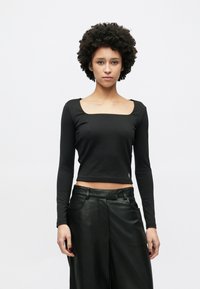 Haut court noir  à manches longues avec un décolleté carré, en tissu doux. Associé à un pantalon en cuir noir taille haute.