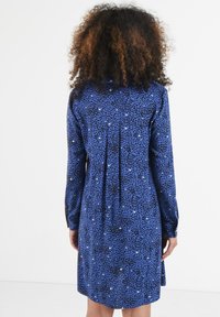 Blaues Kleid mit einem gesprenkelten Schwarz-Weiß-Muster. Lange Ärmel, geknöpfte Manschetten und eine Falten-Detail im Rücken. Lässige Passform.