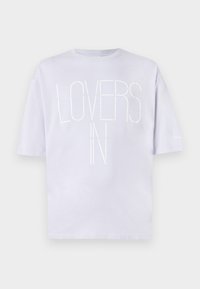 Světle levandulové bavlněné tričko s kulatým výstřihem. Na přední straně vynikající bílý blokový text "LOVERS IN." Krátké rukávy s uvolněným střihem.