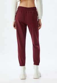 Marron joggers med elastisk talje, med manchetter ved anklerne og en glat tekstur, parret med hvide chunky støvler.