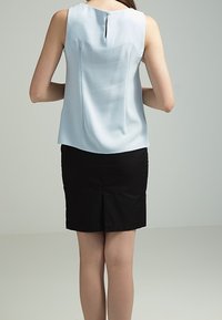 Blusa sin mangas de color azul claro con una sutil textura y detalle de botones en la parte posterior, combinada con una falda negra con abertura.