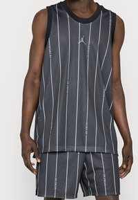 Débardeur de basketball en mesh noir avec des rayures verticales blanches et le texte "Air Jordan", associé à un short assorti affichant le même motif.