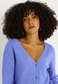 Cardigan de punto color lavanda con escote en V profundo, textura acanalada, bordes plateados a lo largo del escote y dos botones en la parte delantera.