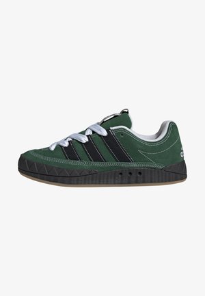 Baskets en daim vert avec des rayures noires, des lacets blancs, et une semelle noire texturée, vues de côté sur un fond blanc.