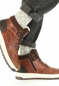 Baskets montantes en cuir marron avec des accents texturés et une semelle blanche. Comprend une fermeture éclair sur le côté, un laçage et des chaussettes en maille grise.