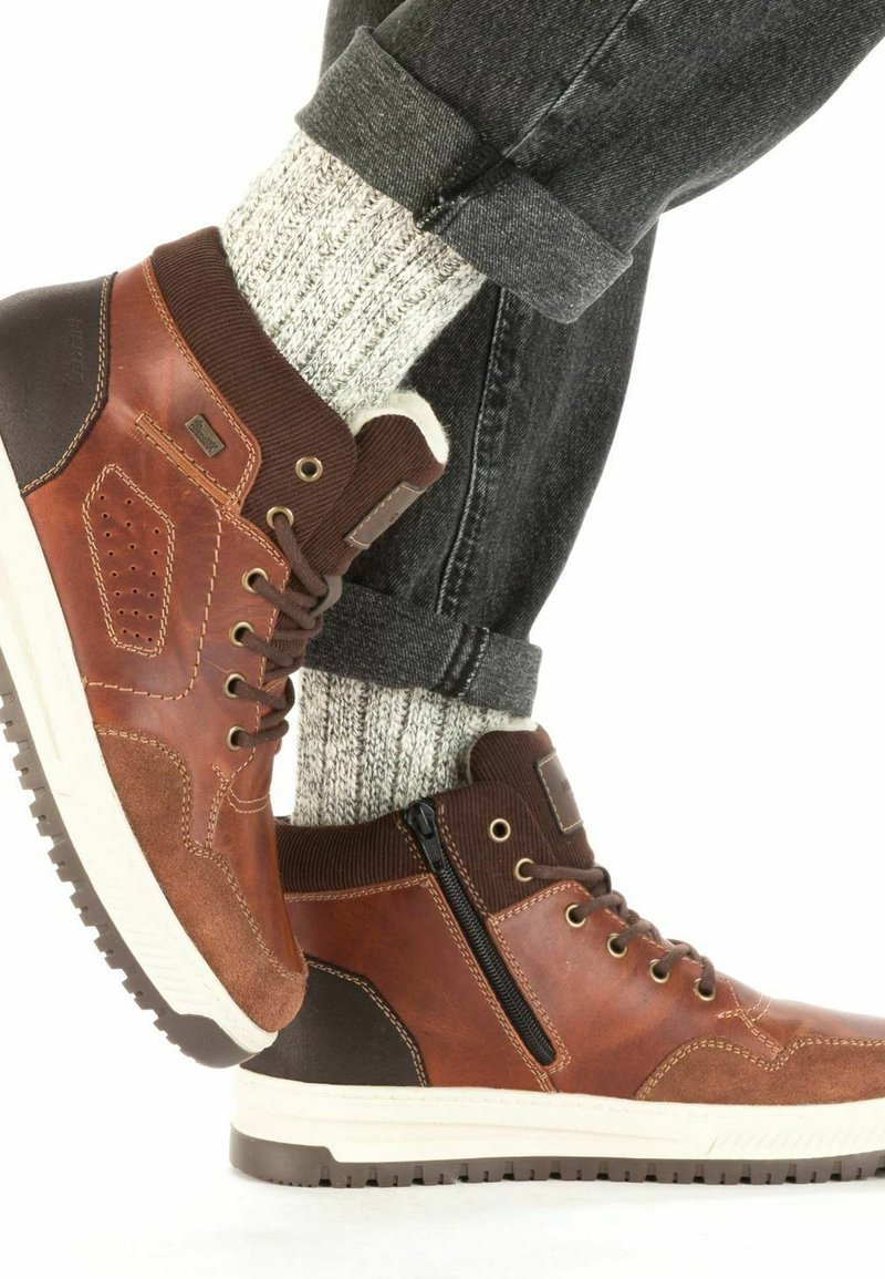 Baskets montantes en cuir marron avec des accents texturés et une semelle blanche. Comprend une fermeture éclair sur le côté, un laçage et des chaussettes en maille grise.
