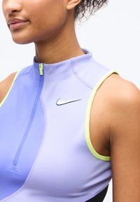 Κοντινό πλάνο γυναίκας που φοράει αμάνικο αθλητικό τοπ σε λεβαντί απόχρωση με μπροστινό φερμουάρ και μαύρο λογότυπο Nike στο στήθος.