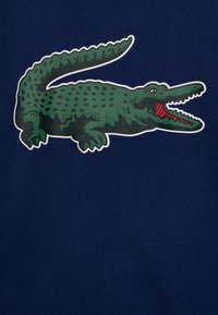 Marineblått tyg med en stor grön krokodilmönster med mörka prickar, öppen mun och röda accenter.