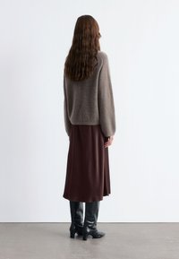Brauner Wollpullover, kastanienbrauner Satinrock und schwarze Krokodilprägung Kniestrumpfstiefel. Glatte Texturen, lockere Passform und leichter Saum.
