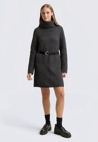 Donkergrijze gebreide coljurk met lange geribde mouwen, in de taille afgebonden met een zwarte band, gecombineerd met zwarte plateauzolen.