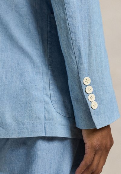 Ανοιχτό μπλε, υφασμάτινο σακάκι με υφή, με μία σχισμή και τέσσερα εκρού κουμπιά στο μανίκι. Είναι ορατές λεπτομέρειες της υφής του υφάσματος.