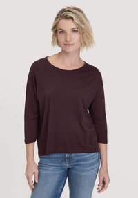 Burgunderfarbendes Langarmshirt mit lockerer Passform, Rundhalsausschnitt und weichem Stoff. Kombiniert mit blauen Jeans in einem lässigen Stil.
