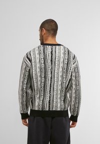 Strickpullover in Übergröße mit vertikalen Mustern in Schwarz, Weiß und Grau. Gerippte schwarze Bündchen und Saum, strukturierter Stoff mit unterschiedlichen Streifenmustern.