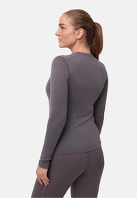 Graues langärmliges Oberteil mit figurbetontem Design, rundem Ausschnitt und glatter Textur. Kombiniert mit passenden grauen Leggings.