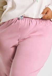 Różowe spodnie z elastycznym paskiem w talii mają gładką fakturę i ozdobę w postaci kolorowej kokardy na pasku. Casualowy design.