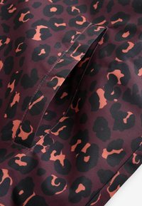 Lähivõte taskust riidel, millel on burgundia, musta ja oranži gepardi triibuline muster.