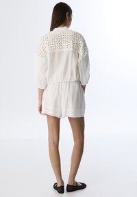 Collant blanc avec un dos en crochet texturé, des manches courtes et une taille élastique. Tissu lisse avec une coupe décontractée. Chaussures plates noires.
