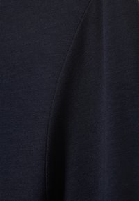 Tmavomodrá látka s jemnou, nenápadnou väzbou, ktorá má hladký povrch a jemný lesk. Detailný záber sa zameriava na šev.