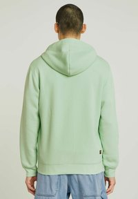 Haut à capuche vert menthe avec un cordon de serrage, des poignets côtelés et un ourlet inférieur. Tissu doux, coupe décontractée, et étiquette de marque sur le côté inférieur gauche.