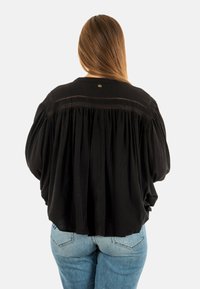 Blusa nera oversize con dettagli arricciati sul retro, maniche lunghe e un piccolo bottone rotondo decorativo al colletto. Tessuto testurizzato.