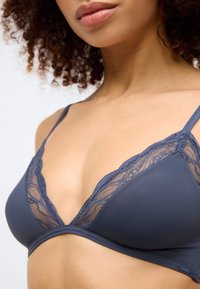 Soutien-gorge triangle bleu foncé en tissu lisse avec des accents en dentelle le long du décolleté. La dentelle présente un motif floral et des bretelles réglables.