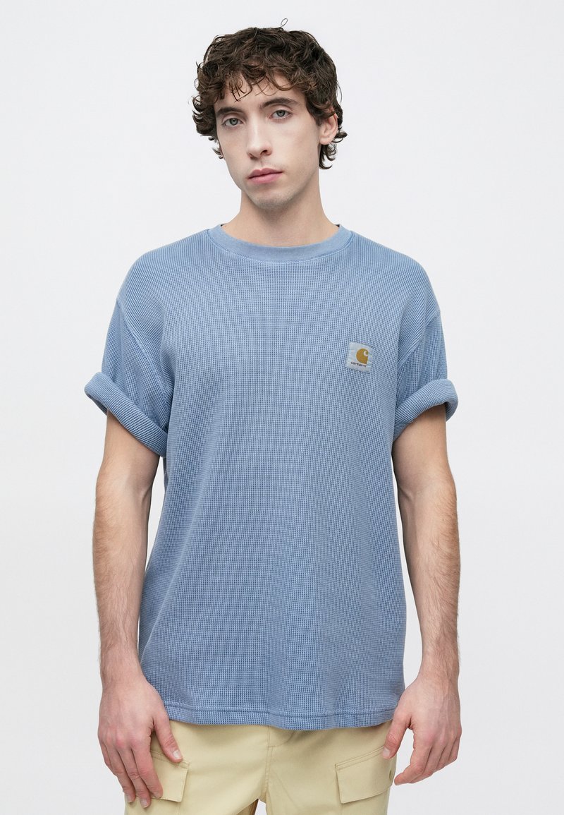 Light blue, short-sleeve, crewneck t-shirt in textured fabric with rolled cuffs and a small logo patch on the chest. Cotton material.