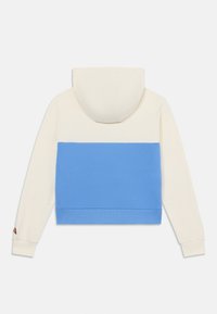 Hoodie accorciato, presenta una parte superiore crema e un fondo a coste blu. Tessuto testurizzato con cappuccio e polsini a coste coordinati. Logo sulla manica.