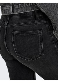 Gros plan sur la poche arrière et la ceinture d’un jean en denim noir avec un patch en cuir noir de la marque, assorti à une veste en denim noir.