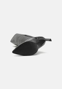 Bottine en cuir noir avec un bout pointu, un dessus texturé, une fermeture à glissière sur le côté et un talon plat. La surface semble lisse et élégante.