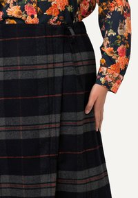 Woll-Plaid-Rock in Marineblau mit grauen und roten Streifen. Verfügt über seitliche Taschen und einen flachen Bund. Kombiniert mit einem floral gemusterten Langarmhemd.