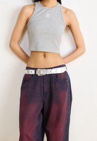 Grå kort t-shirt med rund halsringning och logotyp, tillsammans med mörklila jeans med ett vitt nitarbälte och fickor.