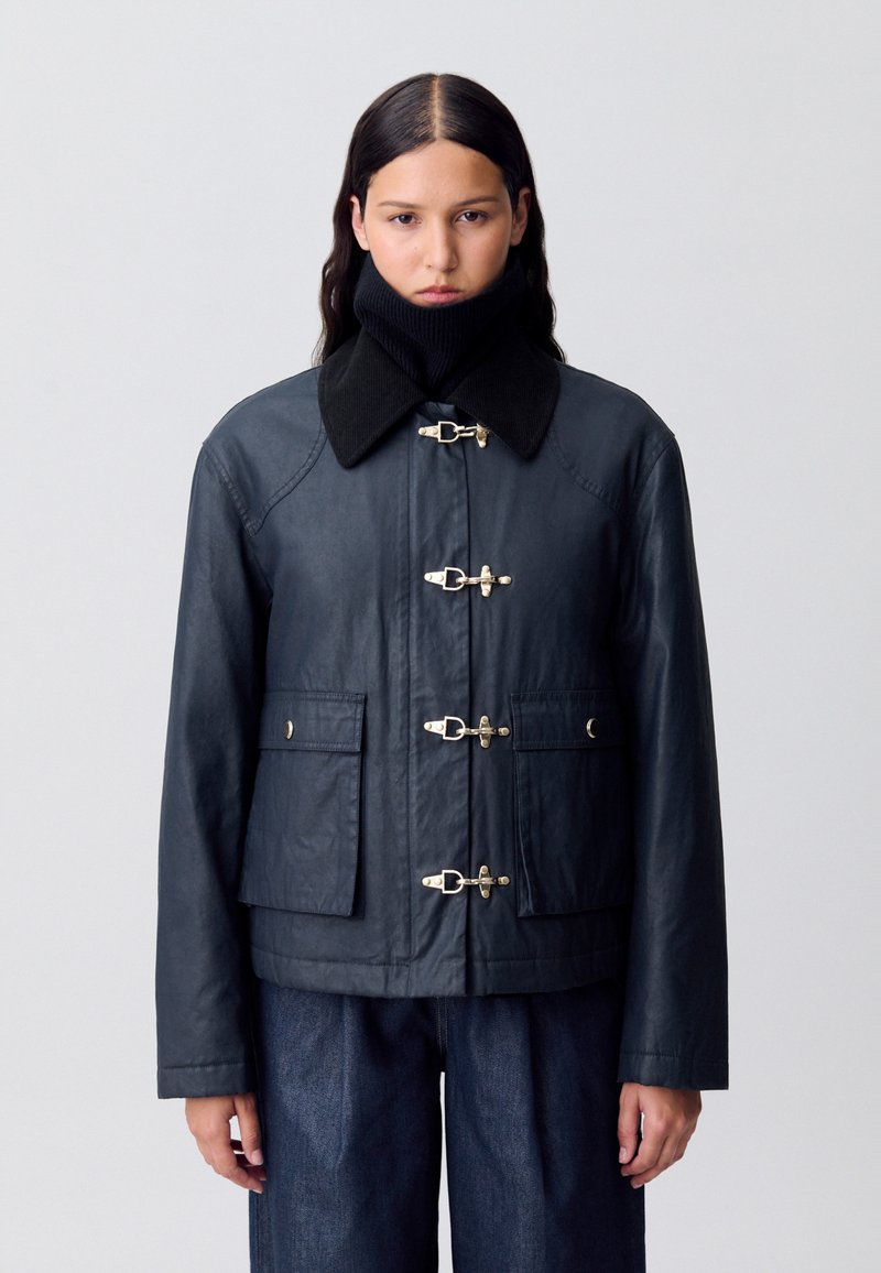 Veste imperméable bleu marine, avec un col noir, des fermetures à cordon, et deux poches avant. Fabriquée dans un matériau lisse et durable.