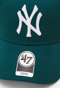Groene baseballpet met een verhoogd wit geborduurd "NY" logo, een textiele stofoppervlak, en een zwart-wit label met '47 en OSFA.