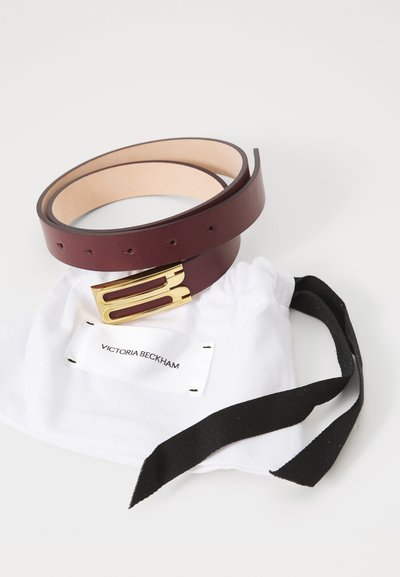 Curea din piele de culoare burgundy cu o cataramă aurie, asociată cu un săculeț din bumbac alb, având un șnur negru și etichetă.