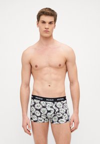 Fekete boxer alsónadrág fehér és zöld margarétás mintával, amelynek szilárd fekete derékpántján "HUGO" felirat található. Puha, rugalmas anyag.