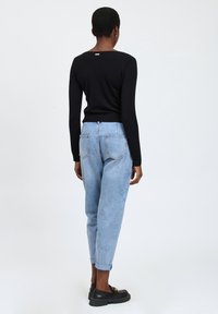 Schwarzes Langarmshirt mit geripptem Saum, kombiniert mit hellblauen, tapered Jeans mit umgeschlagenem Saum und zwei Gesäßtaschen, getragen mit schwarzen Schuhen.