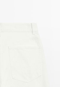 Vista posteriore di jeans in denim bianco che mostrano una singola tasca posteriore, passante per cintura e vita su sfondo bianco.