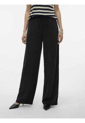 Pantalons larges noirs avec une taille à cordon, présentant une texture lisse et associés à des escarpins noirs à bout pointu.