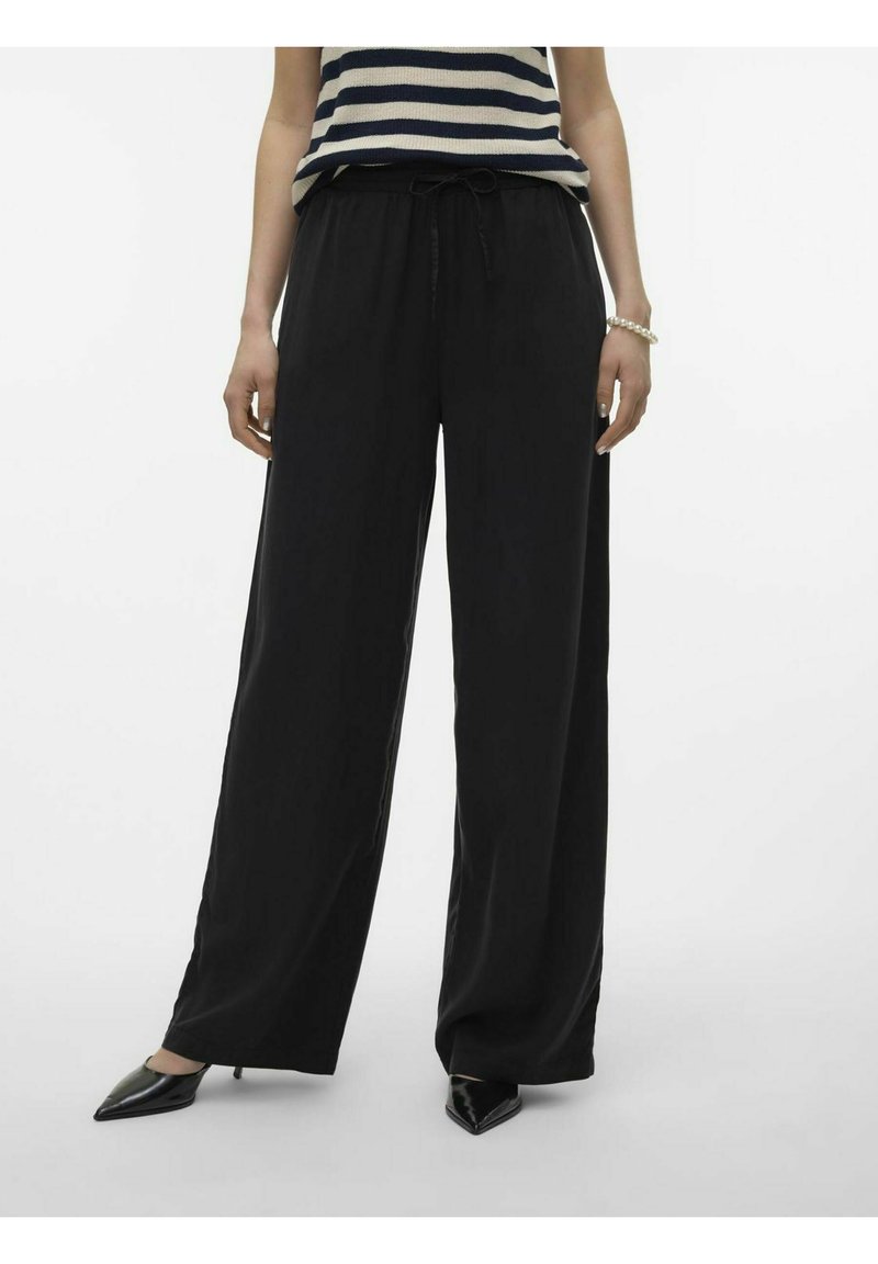 Pantalons larges noirs avec une taille à cordon, présentant une texture lisse et associés à des escarpins noirs à bout pointu.