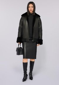 Czarna skórzana kurtka z kołnierzem i futrzanym wykończeniem, w połączeniu z dopasowaną skórzaną spódnicą i czarnymi, z wysokością do kolan, botkami na obcasach. Mała czarna torebka.