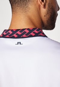 Λευκό πουκάμισο με γιακά σε ναυτικό μπλε και ροζ γεωμετρικό σχέδιο. Μικρό λογότυπο σε μαύρο χρώμα κεντραρισμένο στην πλάτη.