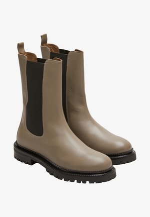 Beige leather Chelsea boots with elastic sides, brown inner lining, and rugged black rubber soles featuring a textured tread pattern.